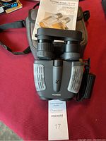 Binoculars with printed manual and carrying case on red surface with auction tag