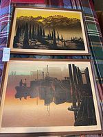 Both framed prints laid out on plaid surface: mountainous scene (top) and dock scene (bottom)