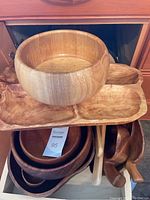 Vintage wooden serving pieces including bowls, a handled wooden bowl on top, stacked bowls underneath, and a small wooden scoop, all in warm-toned wood.