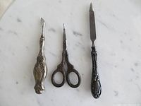 Front view of the three antique silver plated grooming and craft tools: cuticle tool, embroidery scissors, and nail file on marble surface