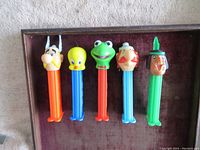 Front view of five PEZ dispensers with character heads: Viking, Tweety Bird, Kermit the Frog, Scotsman, Indigenous figure in a row from left to right on a brown surface