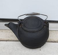 Front and side view of antique cast iron tea kettle showing metal handle with coil grip and spout shape.