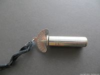 Cylindrical metal pipe tuner with engraved chromatic scale letters on an attached fan-shaped plate, along with a black fabric strap.