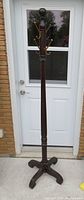 Full view of the antique coat hanger stand showing the entire height and metal hooks at the top against a door background.