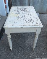 Top angled view showing worn white paint and wood beneath on table surface and leg details.