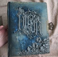 Front cover of the blue velvet Victorian photo album displaying detailed ornate metal floral and butterfly decorations and a side metal clasp.