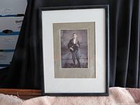 Frontal view of the framed black and white photo showing the violinist standing, holding a violin. The photo is mounted on a gray mat and enclosed in a black frame with white matting.