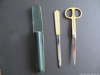 Photo showing a gold-colored letter opener, gold-colored scissors, and a green sheath holder against a dark background.