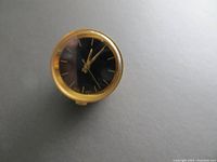 Close-up of the watch face with black dial, gold hands, and hour markers, showing the manual winding crown at the bottom edge.