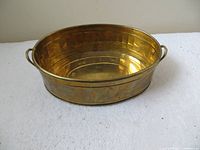 Oval polished brass planter shown from front angle with reflective golden surface and side handles.