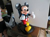 Front-side view of vintage Mickey Mouse figure telephone showing thumbs-up pose and hiking backpack handset.