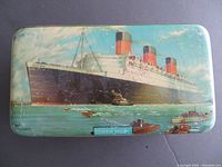 Top lid showing detailed illustration of the R.M.S. Queen Mary ship with tug boats on water and sky background.