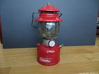 Full view of vintage red Coleman lantern model 200A showing red metal body, glass globe, and black metal handle.