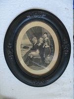 Photo of the 19th-century etching of George Washington and family in carved black oval wood frame with floral decorations. The image shows the overall framed artwork.