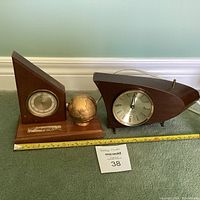 Photo showing two vintage wooden clocks side by side with measuring tape beneath and lot card