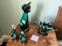 Three Blue Mountain Pottery items on a wood surface: tall cat figurine, two duck figurines, and seashell vase planter.