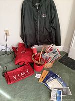 Photo showing two Canada travel jackets labeled 'Return to Vimy' and 'Vimy' with a collection of Canada hand flags, brochures, a red container, and wicker basket arranged on the floor.