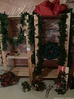 Full view of garland hanging on wooden shelves with wreaths below and basket arrangement visible on bottom shelf.