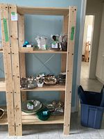 Wooden IKEA shelf with multiple tiers, natural wood finish, some small scratches and holes on the sides, shown with unrelated items on shelves.