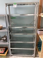 Front view of the metal shelving unit showing six flat metal shelves supported by vertical posts with adjustment holes, against a neutral background.