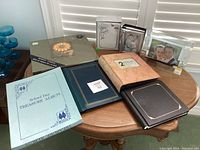 Wide view of six photo albums and three picture frames arranged on a table.