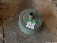 Top-down view of the round cement umbrella stand showing the central cylindrical holder with a clamp and the overall wear on the surface.