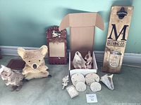Full lot view showing two stuffed animals (koala and kangaroo), several shells including conch shells and sand dollars, a small coral piece, a wooden decorative piece with a bear image, and a wall-mounted bottle opener.