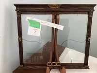 Full view of vintage wooden frame showing ornate top detailing, gilded accents, and the overall rectangular shape with glass front panel that has a long crack.