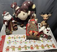 Photo showing assorted Christmas decorations including Santa figurine, elf doll in knit outfit, sleeping child figurine, reindeer figure, fireplace figurine, and a sheet of Christmas-themed stickers.