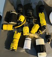 Photo showing 14 assorted electrical plug ends of various types and colors (black and yellow) in unknown condition.