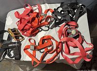Photo of six assorted ratchet tie-down straps in red, orange, and black colors with metal ratchet handles and hooks on a white surface.