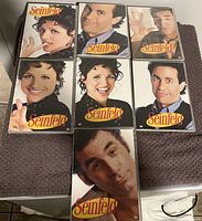 Seven assorted Seinfeld DVD cases displayed on a towel, each with different cast member images on the cover.