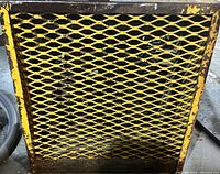 Yellow metal mesh grille front on rectangular commercial heater in metal frame showing some rust and wear.