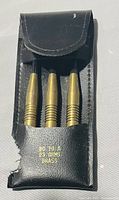 Front view of the black leather or faux leather case holding three brass darts, showing weight and material stamping 'BD 10 A 23 GRMS BRASS'