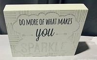 White rectangular wooden decorative block with an inspirational quote in black and glittery silver text.