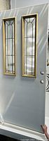 Full view of the white exterior door showing two vertical glass inserts with decorative patterned glass framed in gold trim.