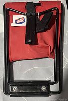 Close-up of folded folding pocket camp chair showing red fabric and black metal frame with strap and Pocket Chair tag.