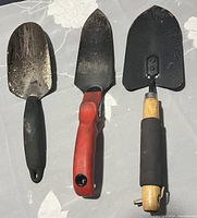 Three garden hand trowels with varied handle types and blade finishes laid on a textile surface.