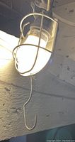 Illuminated hanging work light with metal protective cage and hook, mounted on a wooden surface.
