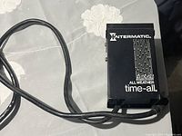 Top view of the black Intermatic All Weather Time-All timer showing the branded front panel and attached power cord.