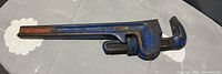 Photo of a large blue metal pipe wrench with adjustable jaws showing some rust and wear.