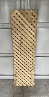Photo of a single wooden lattice panel standing upright against a wall. The lattice is made of natural wood with a diagonal crisscross pattern forming small square openings.