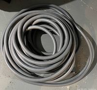Coiled grey flexible conduit hose with corrugated texture.