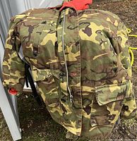 Front view of a camouflage military jacket with a bright red collar, visible zipper and button closure, chest and waist pockets, and adjustable waist tabs.