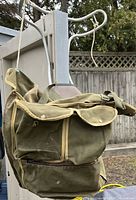 Side view of olive green military knapsack sac made of canvas with several flap pockets and a metal hook attached.