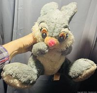 Front view of vintage Disney Thumper plush held up by a hand, showing gray and white furry body, large eyes, and pink nose.