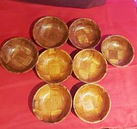 Top view of all eight bamboo salad bowls arranged on a red surface showing the lighter and darker natural wooden tones and woven pattern
