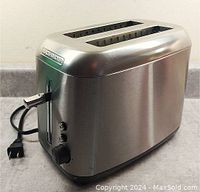 Front and side view showing toaster with stainless steel body with two slots, control lever, function buttons, and dial.