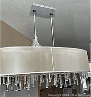 Photo showing the full chandelier suspended from ceiling mounting plate with visible satin drum shade and hanging triangular crystal prisms.