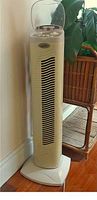 Full tall beige tower fan with vertical vents against wall on wooden floor.